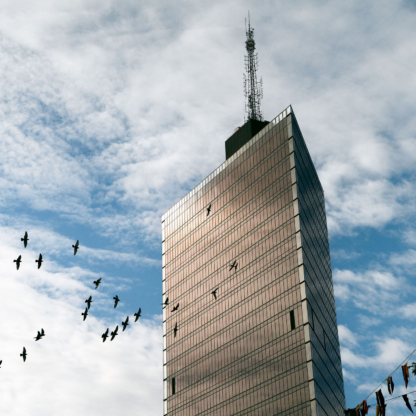 A photo of Kista Science Tower with a background of blue sky with white clowds and silhouettes of a flock of birds flying in front of the tower.